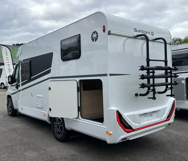Camping-car Sunlight blanc avec porte-vélos, stationné sur un parking.