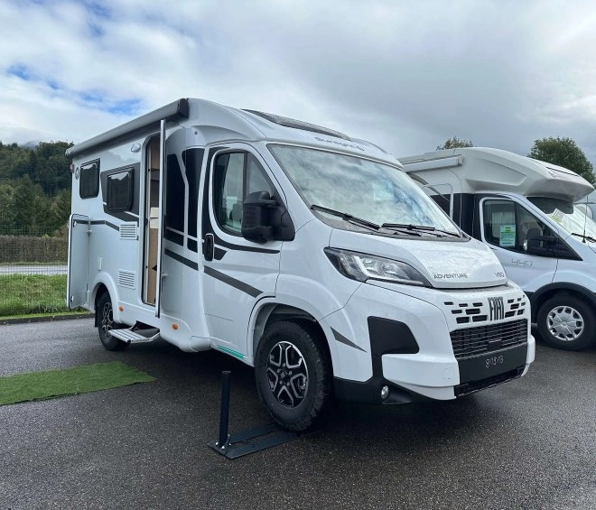 Camping-car blanc stationné sur un parking, porte ouverte, ciel nuageux en arrière-plan