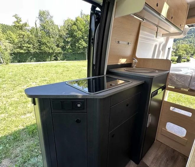 Intérieur d'un camping-car moderne avec cuisine équipée, vue sur l'extérieur verdoyant.