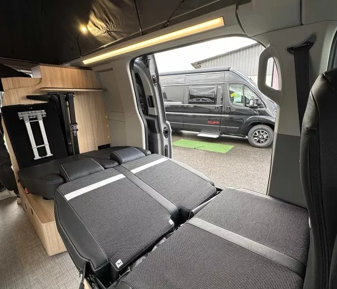 Intérieur d'un van aménagé avec lit déplié et espace de rangement en bois