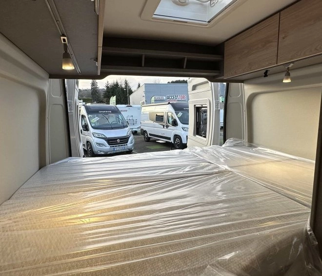 Intérieur d'un camping-car avec lit et vue sur d'autres véhicules stationnés