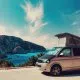 Van aménagé avec toit relevable face à une mer turquoise et falaises