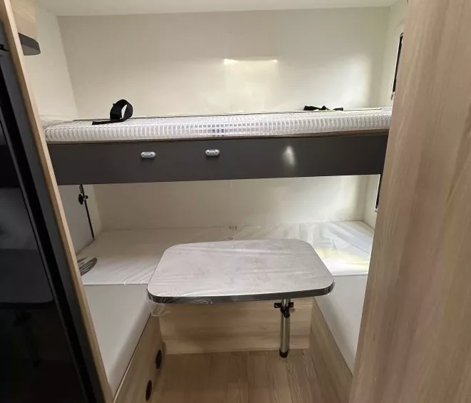 Intérieur d'un camping-car avec lits superposés et table pliante en bois clair.