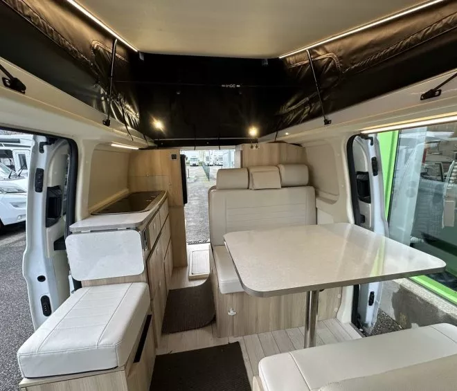 Intérieur d'un van aménagé avec table, banquettes et kitchenette moderne.