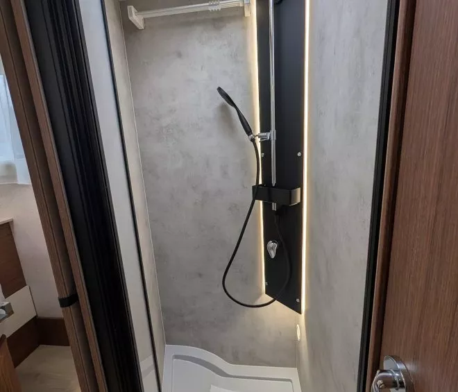 Douche moderne dans un camping-car avec éclairage LED et pommeau noir.
