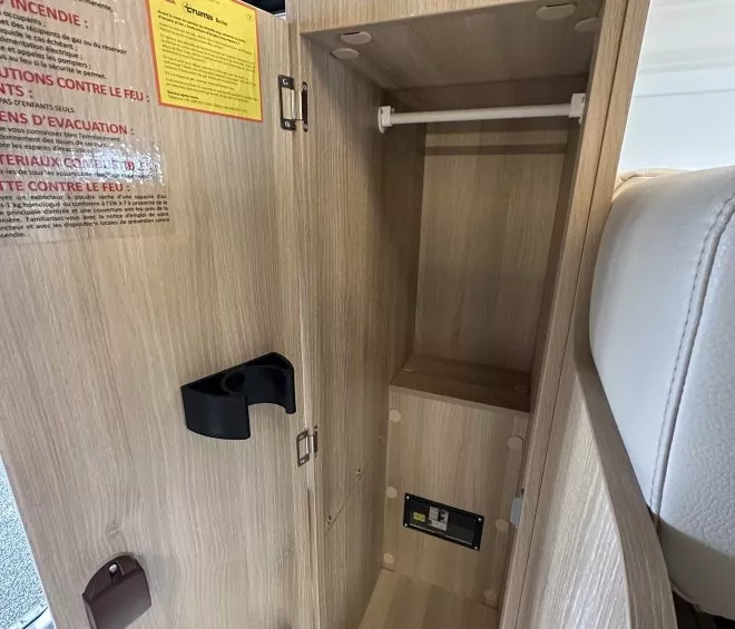 Armoire en bois clair avec étagères et porte ouverte, intérieur de véhicule récréatif.