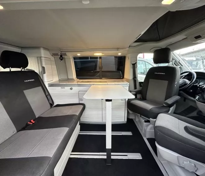 Intérieur d'un van aménagé avec sièges et table pliante, modèle California.