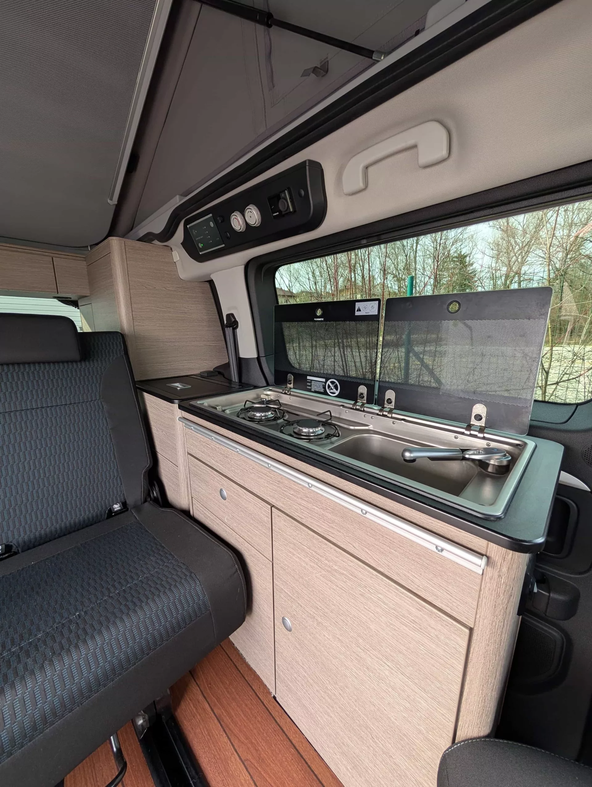 Intérieur d'un van aménagé avec cuisine intégrée et sièges en tissu noir.