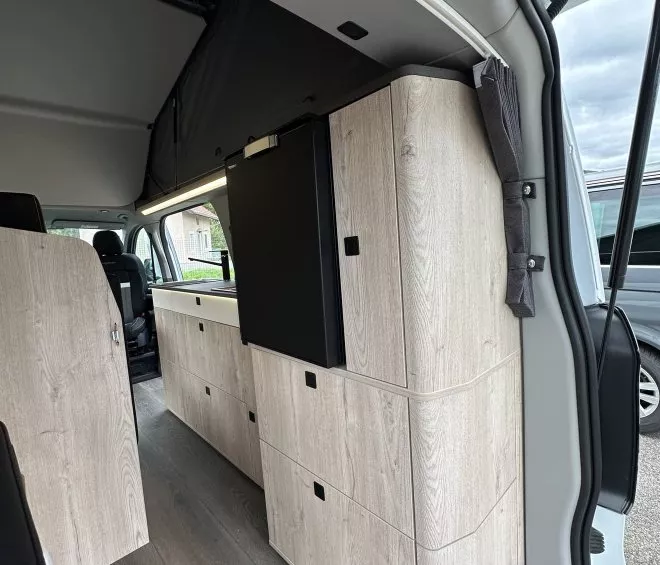 Intérieur d'un van aménagé avec meubles en bois clair et espace de rangement.