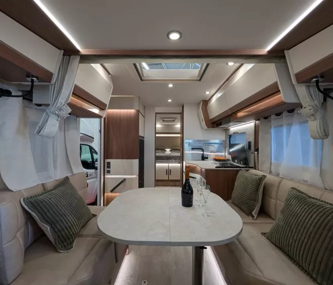 Intérieur moderne d'un camping-car avec table, banquettes et cuisine équipée.