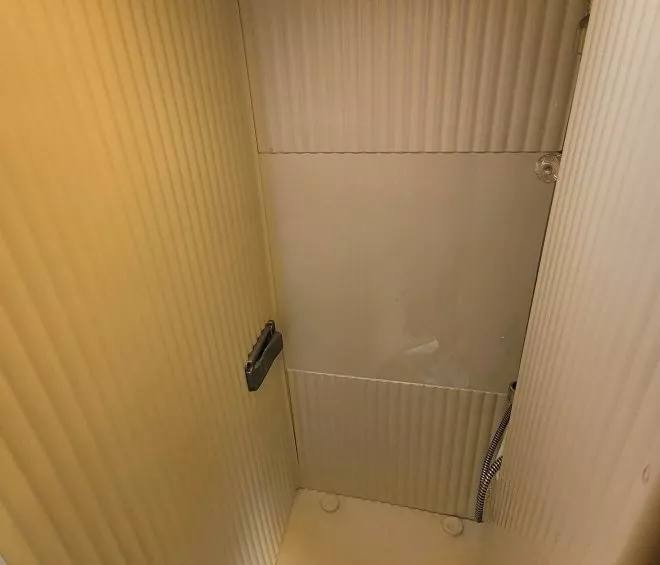 Douche compacte en cabine avec parois en plastique beige et pommeau de douche intégré.