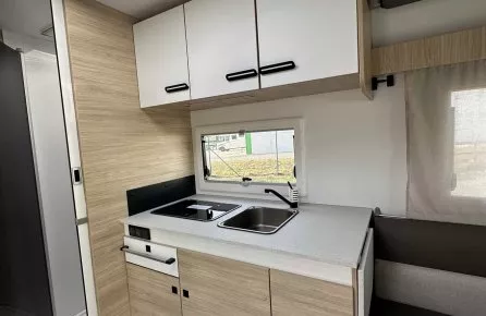 Cuisine moderne de camping-car avec évier, plaques de cuisson et rangements en bois clair.