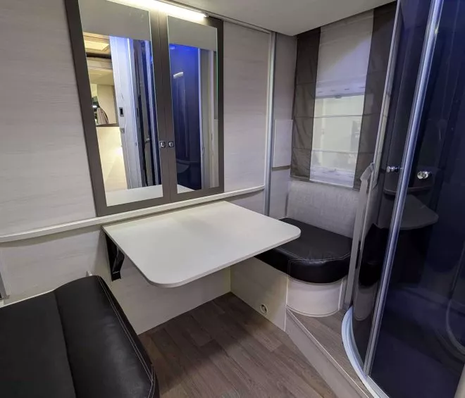Intérieur d'une caravane avec table pliante, banquette et cabine de douche.