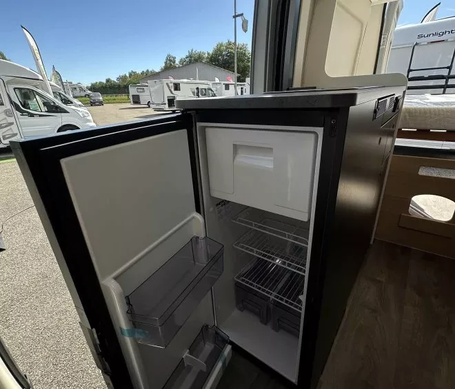 Réfrigérateur ouvert dans un camping-car sur un parking de véhicules de loisirs.