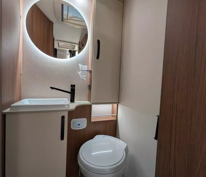 Salle de bain compacte avec lavabo, miroir rond et toilettes modernes dans un camping-car.