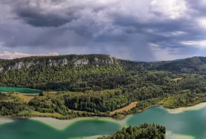 Paysage de lac entouré de forêts sous un ciel nuageux, région montagneuse.