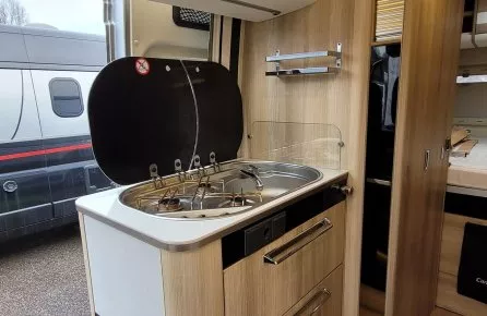 Cuisine compacte en bois dans un camping-car moderne avec plaques de cuisson et rangements.
