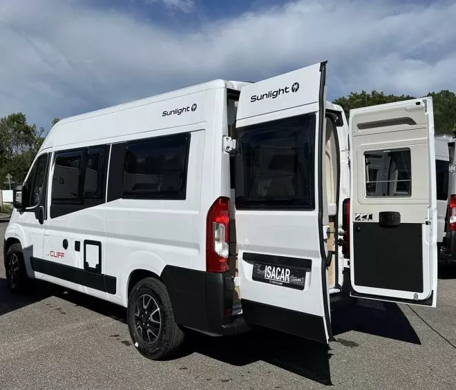 Camping-car Sunlight Cliff blanc avec portes arrière ouvertes sur un parking.
