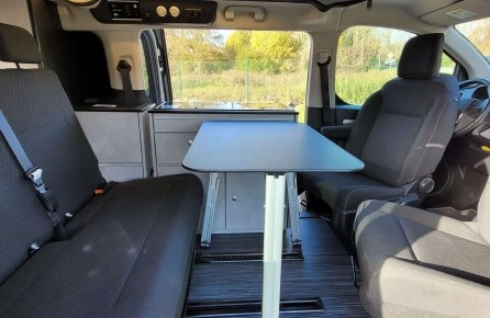Intérieur d'un van aménagé avec table et sièges, vue sur l'extérieur