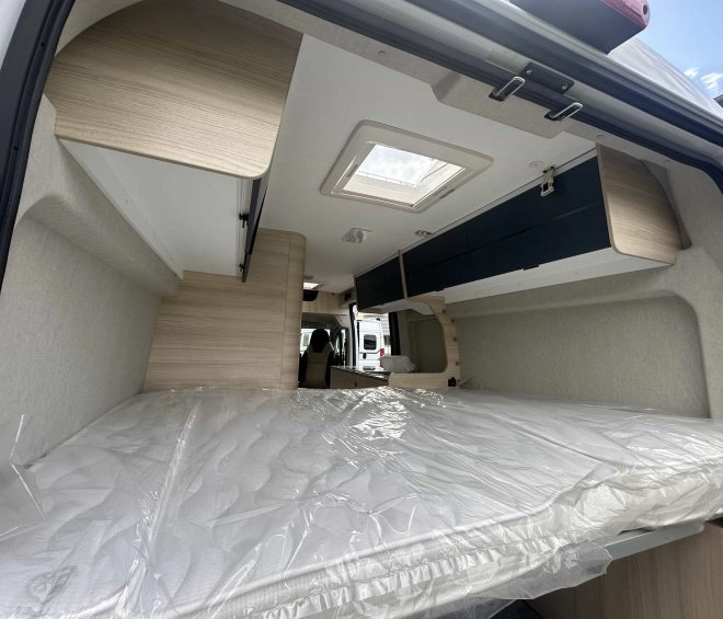 Intérieur d'un van aménagé avec lit et rangements en bois clair.