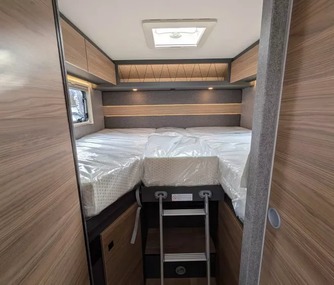Intérieur d'un camping-car avec lit surélevé et échelle, finition bois moderne.