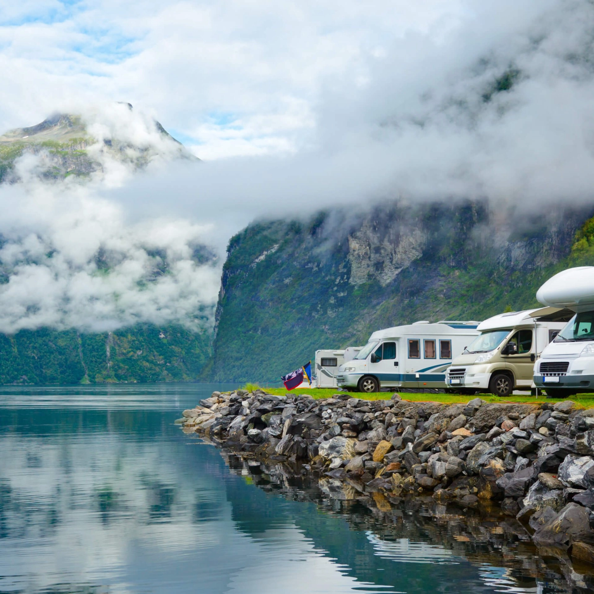 Camping-cars stationnés au bord d'un fjord norvégien avec montagnes et nuages