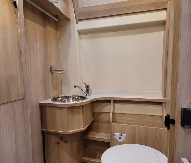 Salle de bain compacte en bois clair avec lavabo et toilettes dans un camping-car.