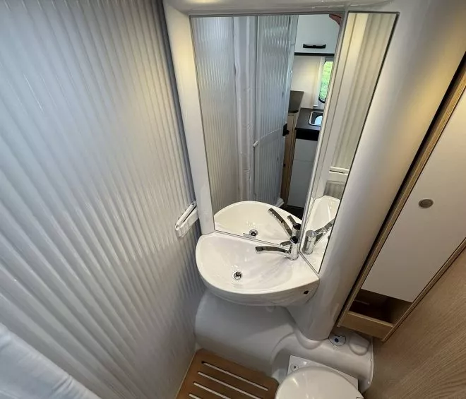 Salle de bain compacte avec lavabo, miroir et toilettes dans un camping-car moderne.