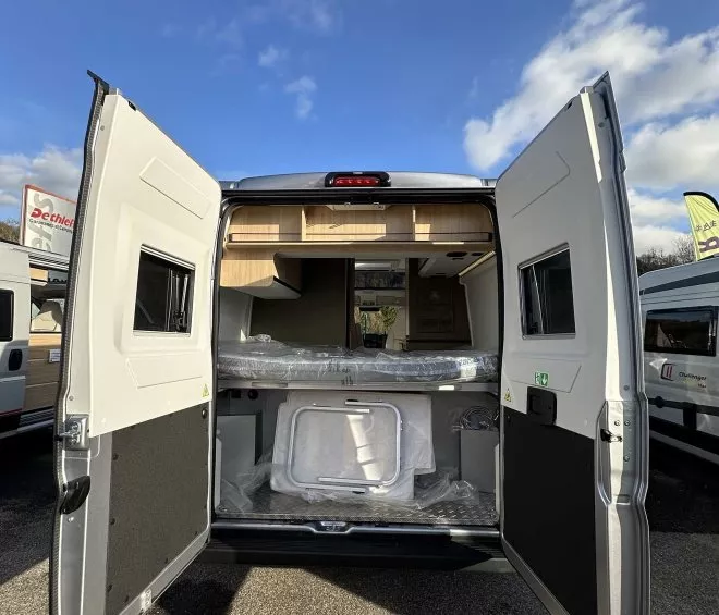 Vue arrière d'un van aménagé avec portes ouvertes sous un ciel bleu.