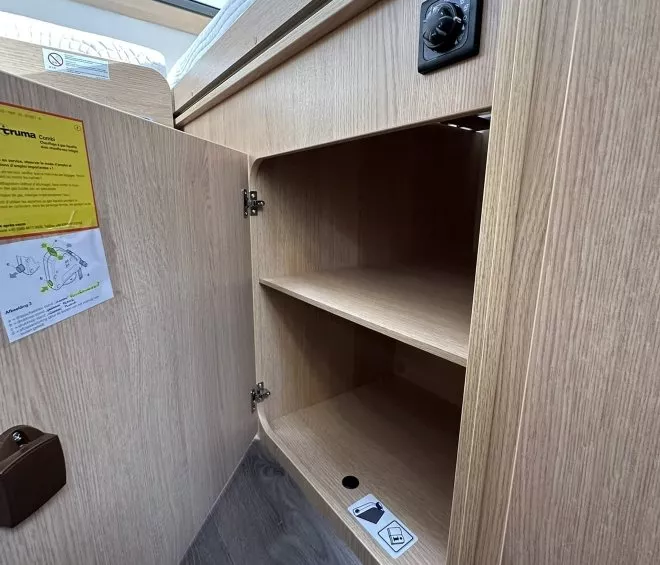 Placard en bois ouvert avec étagères et panneau de commande dans un camping-car.