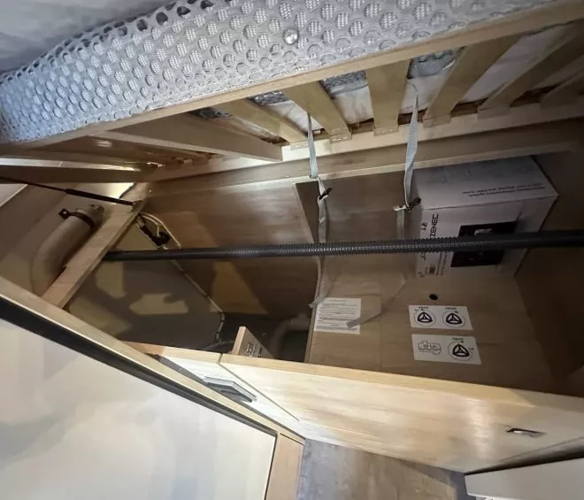 Rangement sous un lit avec tuyaux et boîte en carton dans un espace en bois