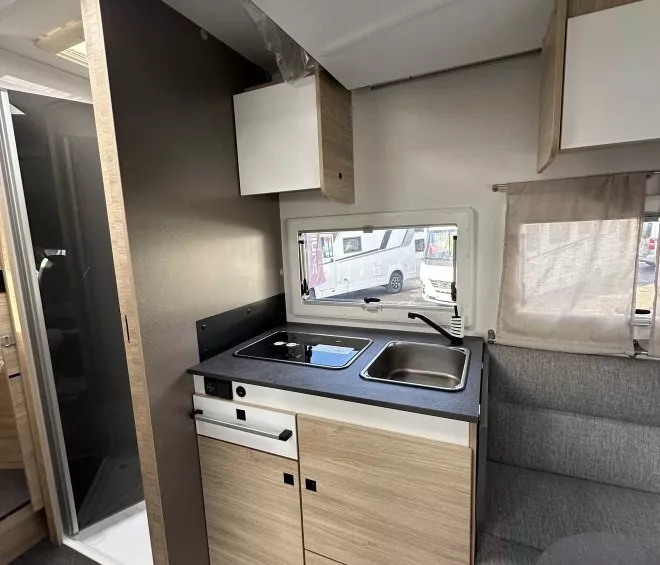Cuisine compacte de caravane avec évier, plaque de cuisson et rangements en bois clair.