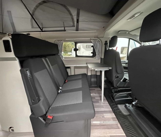 Intérieur d'un van aménagé avec sièges et table pliante, idéal pour le camping.