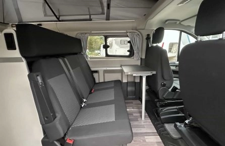 Intérieur d'un van aménagé avec sièges et table pliante, idéal pour le camping.
