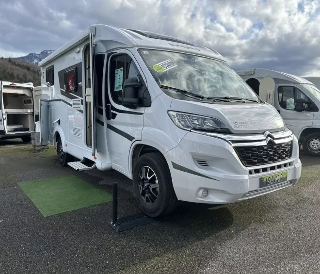 Camping-car Citroën blanc stationné sur un parking, ciel nuageux en arrière-plan.