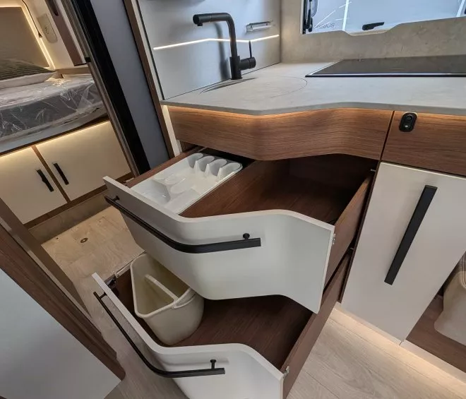 Cuisine moderne de camping-car avec évier, tiroirs ouverts et fenêtre latérale.