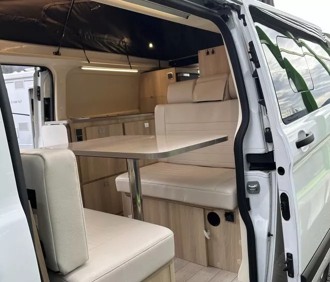 Intérieur d'un van aménagé avec table et banquettes en bois clair.