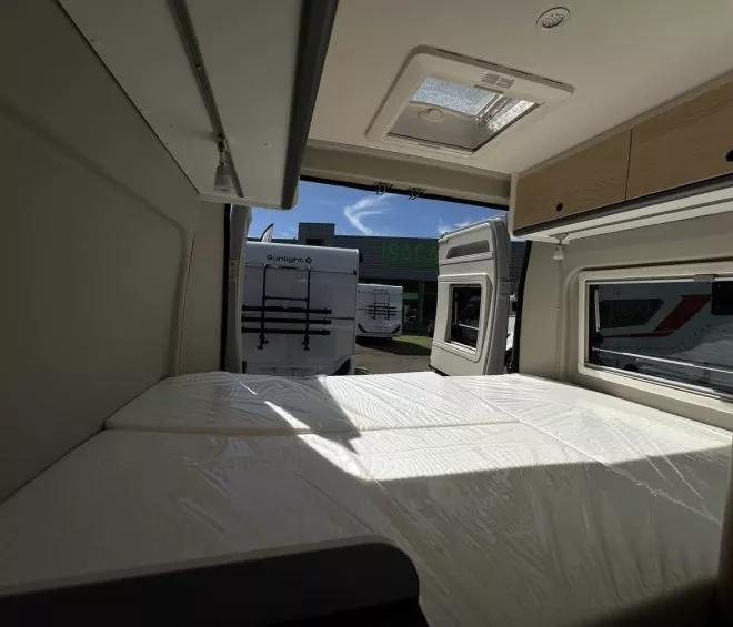 Intérieur d'un camping-car avec lit et rangement, porte arrière ouverte