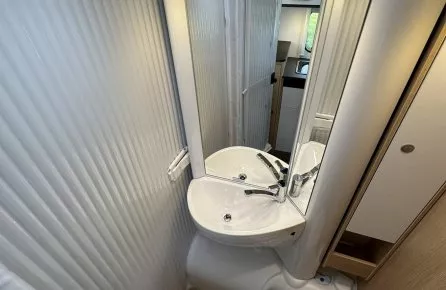 Salle de bain compacte avec lavabo, miroir et toilettes dans un camping-car moderne.