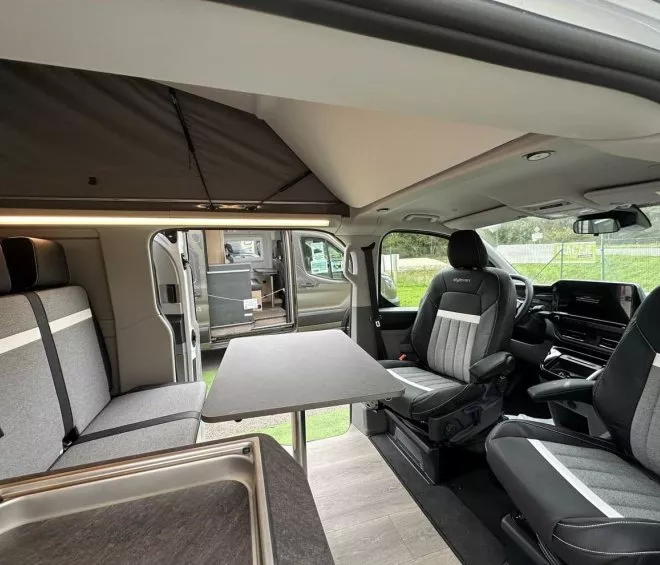 Intérieur d'un van aménagé avec sièges et table pliante, vue sur l'extérieur
