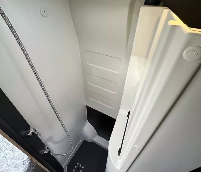 Douche compacte dans un camping-car moderne avec parois blanches et sol antidérapant.