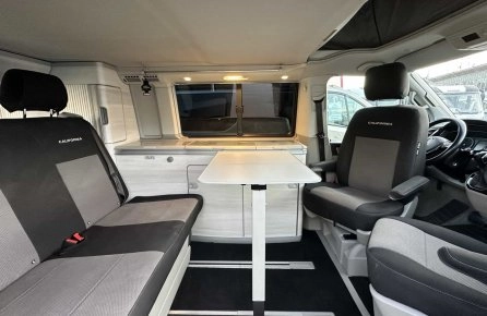 Intérieur d'un van aménagé avec sièges et table pliante, modèle California.