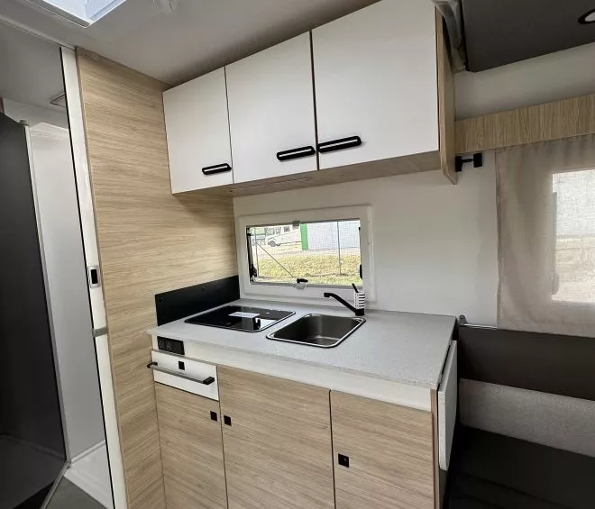 Cuisine moderne de camping-car avec évier, plaques de cuisson et rangements en bois clair.