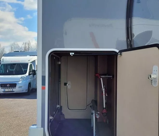 Coffre ouvert d'un camping-car avec rangement pour vélos, ciel bleu en arrière-plan.