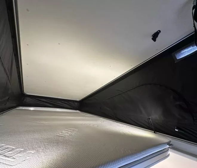 Intérieur d'une tente de toit avec matelas et parois noires, éclairage doux.