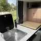 Évier en acier inoxydable dans une kitchenette de camping-car moderne avec planche à découper en bois.
