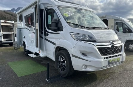 Camping-car Citroën blanc stationné sur un parking, ciel nuageux en arrière-plan.