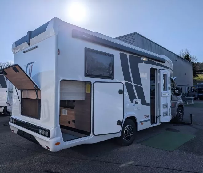 Camping-car blanc stationné avec coffre ouvert, sous un ciel ensoleillé