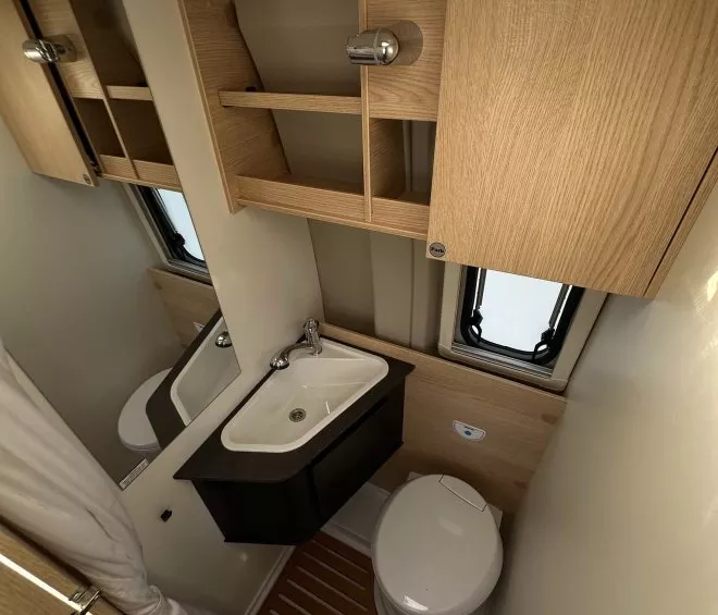 Salle de bain compacte avec lavabo, toilettes et rangements en bois clair dans un camping-car.