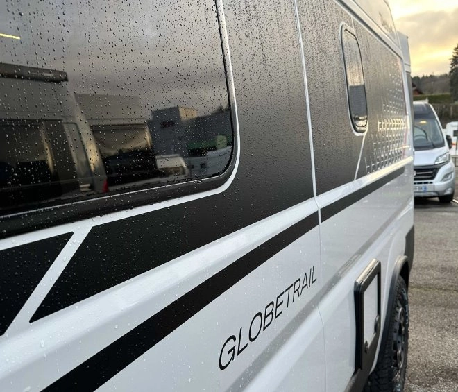 Vue latérale d'un van Globetrail sous la pluie sur un parking.
